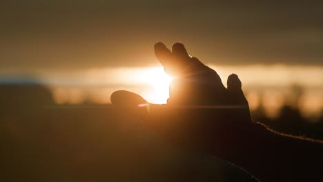 silhouette of right hand reaching for the sun in golden hour sunrise