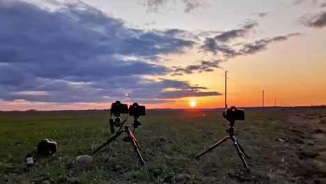 câmeras montadas em tripé preparadas para capturar pôr-do-sol deslumbrante sobre o campo