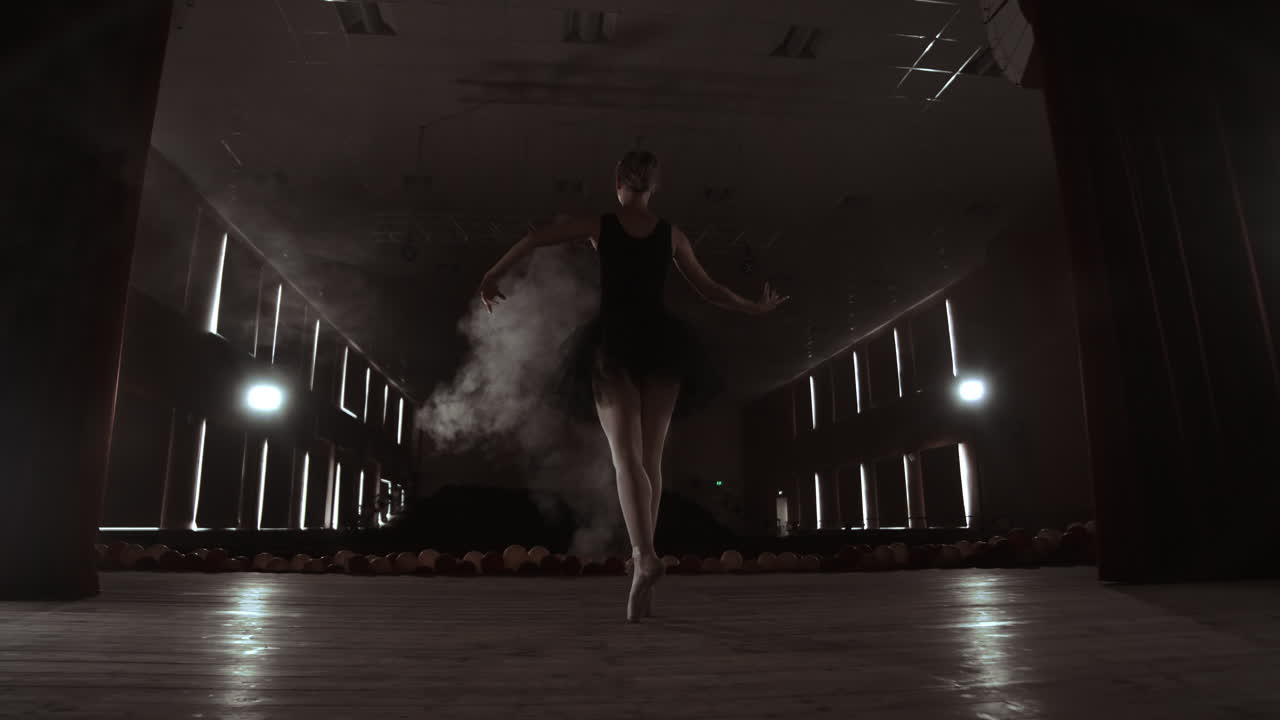A graceful ballerina dancing ballet elements in the dark with light and smoke on the background slow motion
