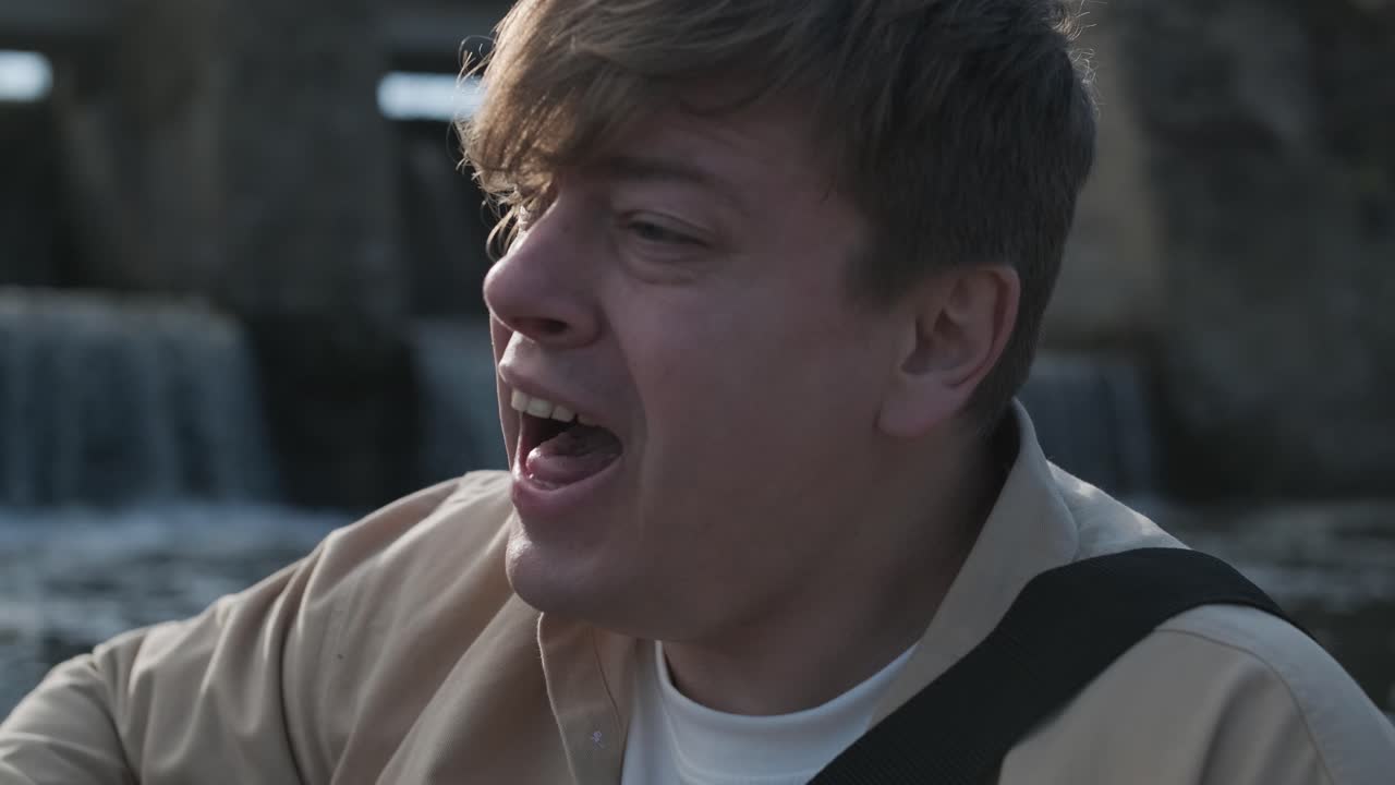 바위의 배경에 산의 강변에 앉아 기타를 연주하는 젊은이. 자유의 개념, 휴식 장소.