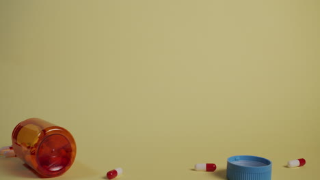 slow motion wide shot of a bottle of pills falling, the lid flies off and pills shoot out