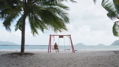 Man-sways-On-A-Swing-Enjoying-The-View-Of-The-An-Hai-Beach-From-Sandy-Shore-In-Con-Dao,-Vietnam