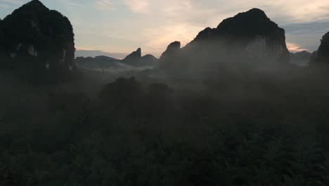 misty morning limestone cliffs rock formations in krabi thailand, flying through mist aerial drone establisher