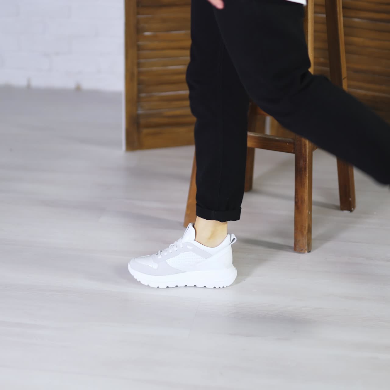 Model jumping high to show white spot shoes. Demonstrating comfortable footwear for everyday activity. Folding screen and tabouret at backdrop