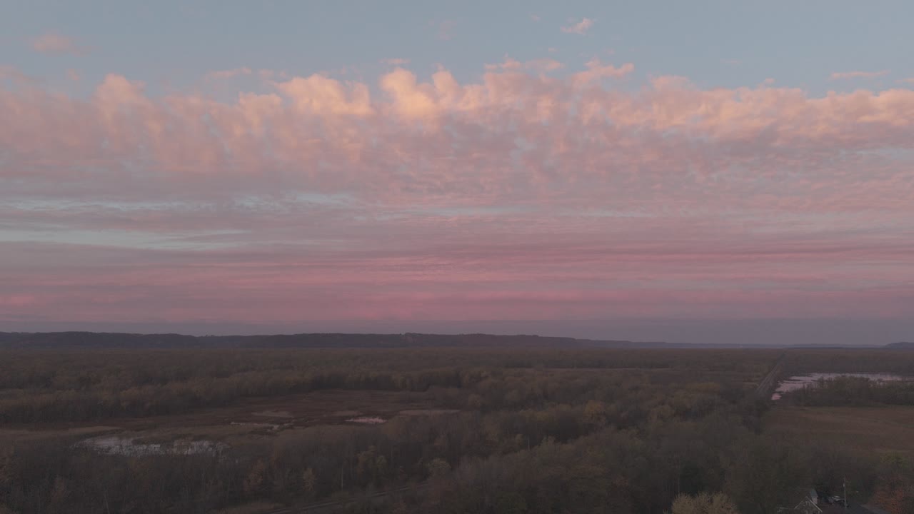 Veduta aerea di una cittadina rurale e di una foresta sotto un cielo rosa al tramonto.