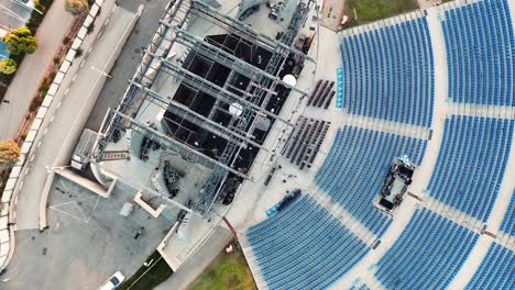 Drone-rotating-shot-flying-above-an-ancient-amphitheater,-huge-stage-with-giant-screen,-grass-and-seats,-golden-hour-Israel