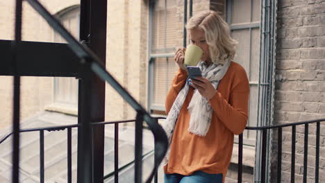 hermosa mujer rubia usando un teléfono inteligente afuera bebiendo café en un descanso