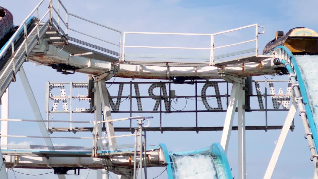 A log flume ride vehicle travels across a high metal track against a blue sky