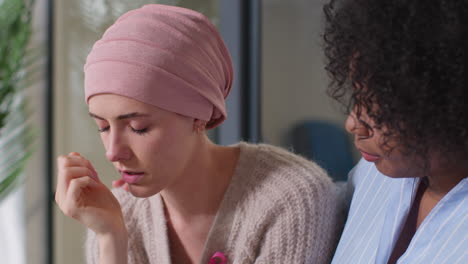 upset young woman patient wearing headscarf receiving chemotherapy treatment for breast cancer being comforted by female patient 1