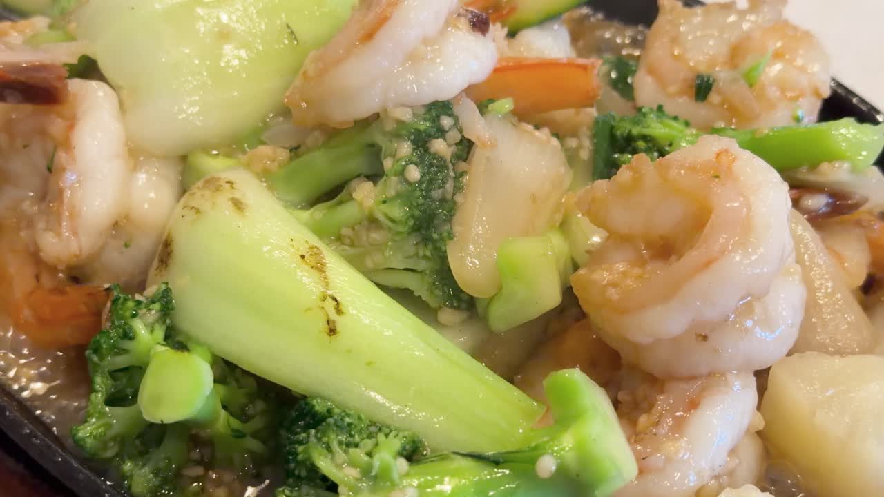 Close-up of hot prawn stir fry with vegetables on a sizzling plate, bright natural lighting