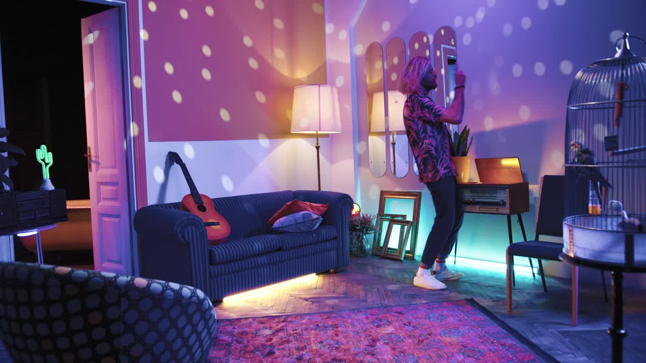 복고풍 테이프 레코더를 켜고 집에서 복고풍 파티에서 정력적으로 춤을 추는 긴 머리를 가진 젊은 세련된 백인 남자