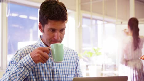 ejecutivo de negocios masculino tomando café mientras usa una computadora portátil