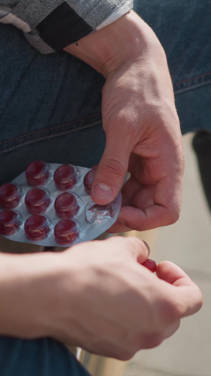 Close up of person hands holding and opening blister packs containing red gummies. person wears blue jeans and checkered shirt with focus on texture detail as they interact with multiple