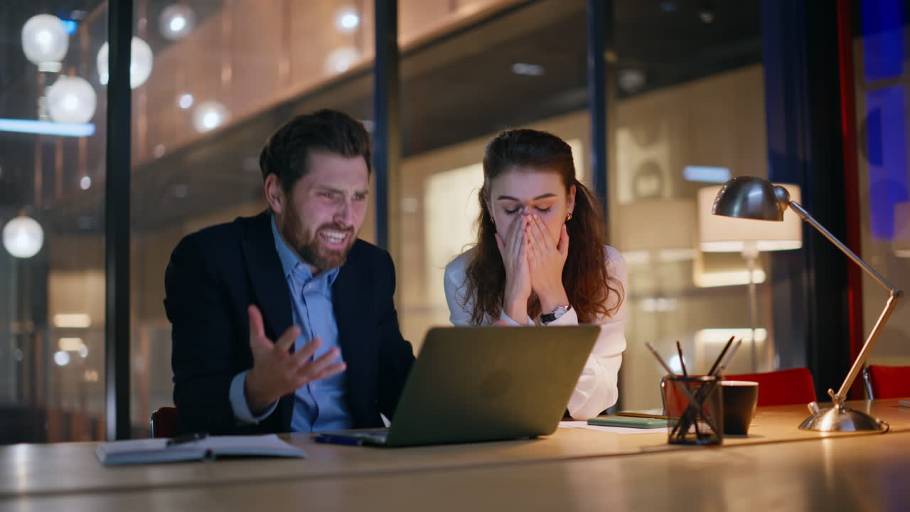 Nervous coworkers closing laptop frustrated project failure at dark office