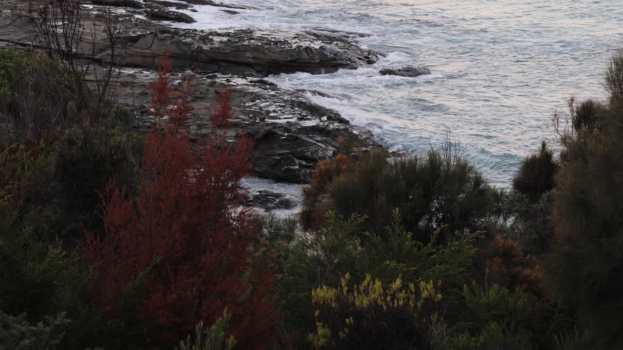 Aerial view of ocean waves moving slowly and crashing into the rocky cliffs