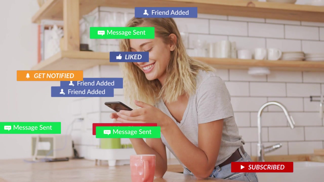 Woman leaning in kitchen holding phone, reading incoming social badges piling over it checking feed