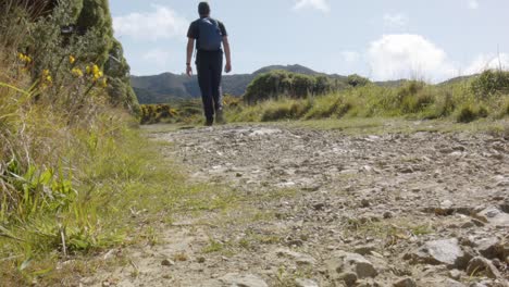 a low angle of a hiker walking away from the camera on a dirt track