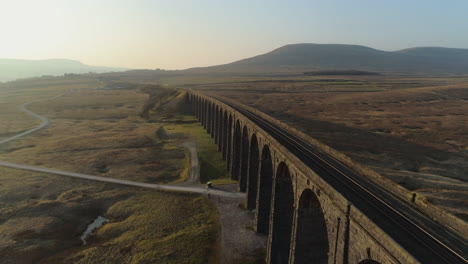 low aerial drone shot closeup to ribblehead viaduct train bridge at stunning sunrise in summer in yorkshire dales england uk with 3 peaks ingleborough mountain in background