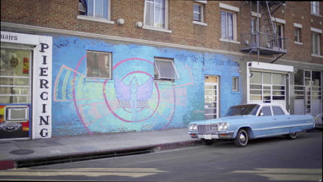 vintage blue car parked beside a building with a colorful mural and piercing sign