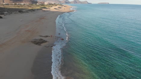 Schöner-Sommerflug-An-Der-Küste-über-Türkisfarbenem,-Klarem-Meerwasser-Mit-Wellen,-Die-Bei-Sonnenuntergang-Am-Sandstrand-Von-Calheta-Rollen,-Portugal,-Overhead-Luftanflug