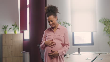 pregnant happy woman posing at camera while touching her belly in the office