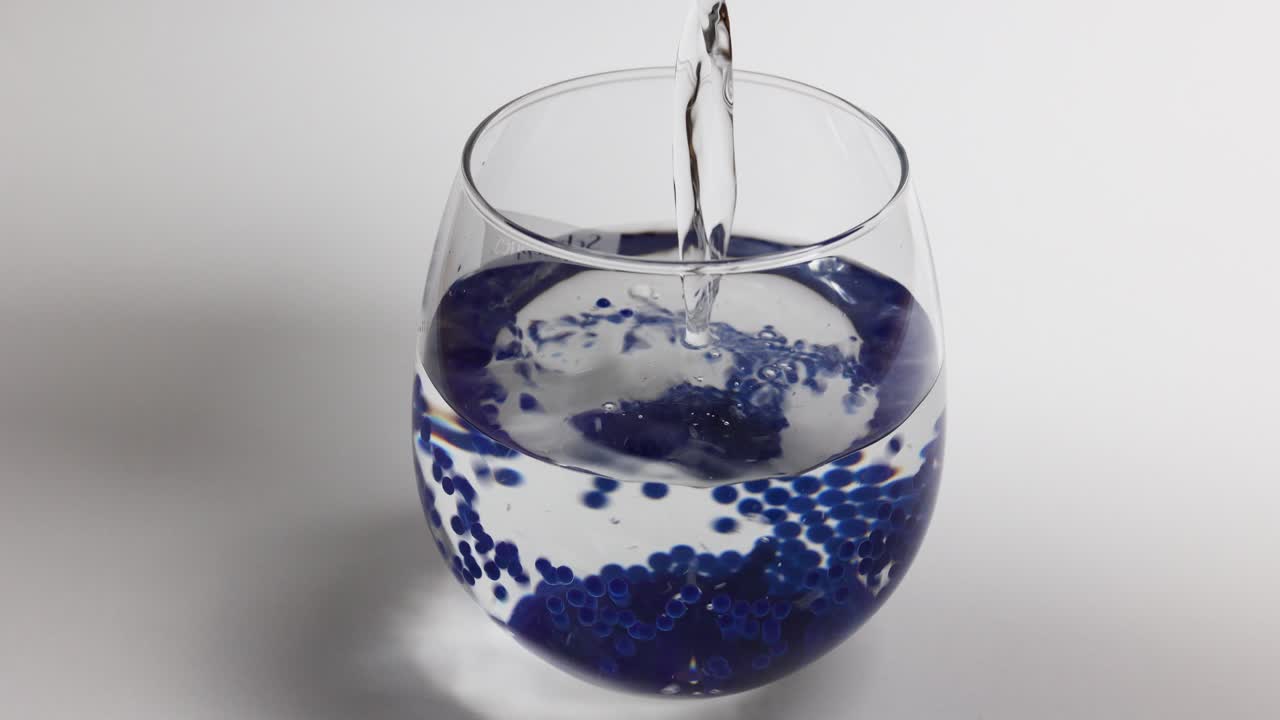 보라색 젤리 구슬이 있는 유리에 깨끗한 물을 붓는다