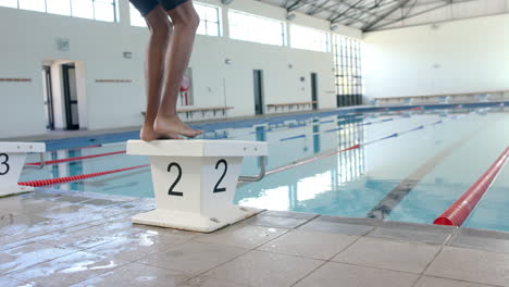 athlete poised on a starting block at a pool, with copy space