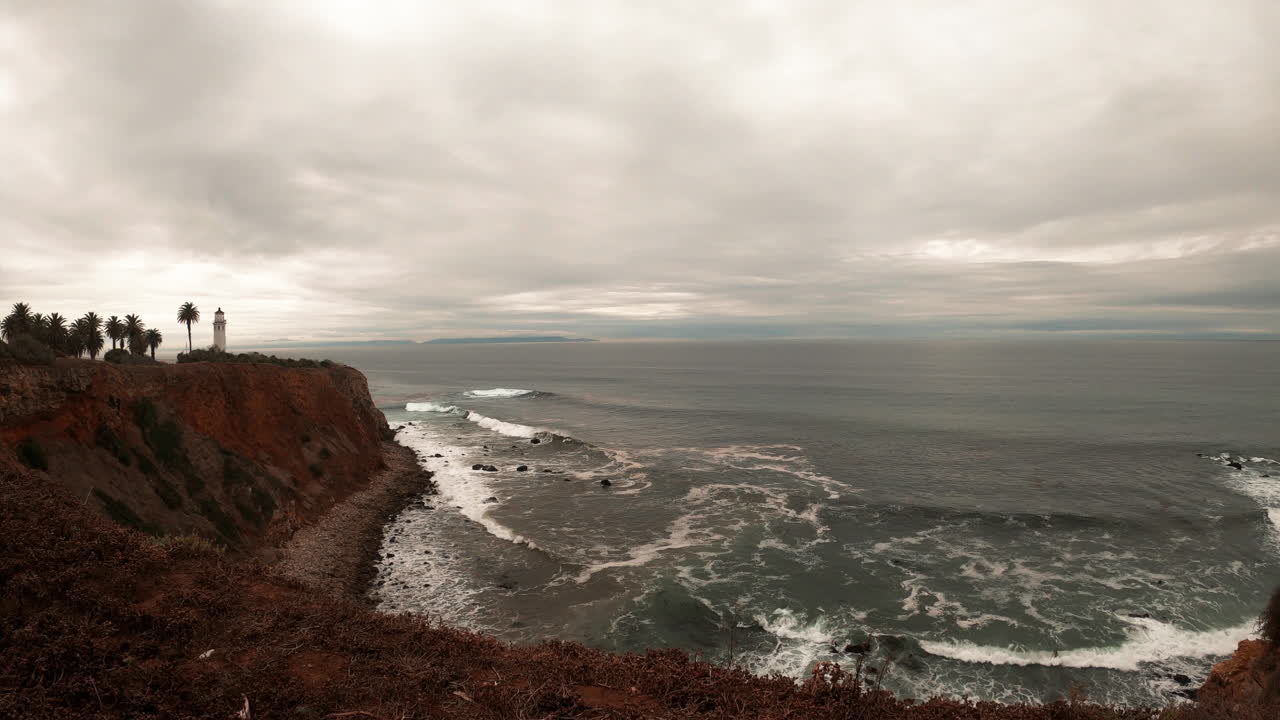 Timelapse da maré oceânica cinzenta de inverno com um farol distante no alto das falésias.