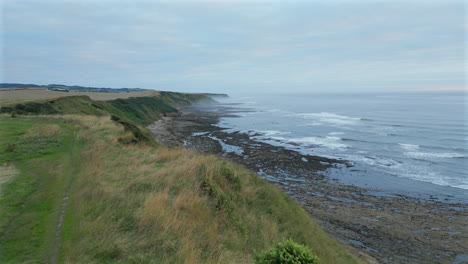 Establishing-Aerial-Drone-Shot-Over-the-Edge-of-Cliff-at-Cleveland-Way-on-North-Yorkshire-Coast-on-Misty-Morning-at-Low-Tide