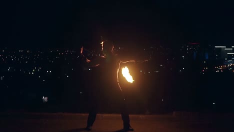 joven hombre rubio hace baile de fuego con dos antorchas gira antorchas en el medio de la noche con el horizonte de la ciudad