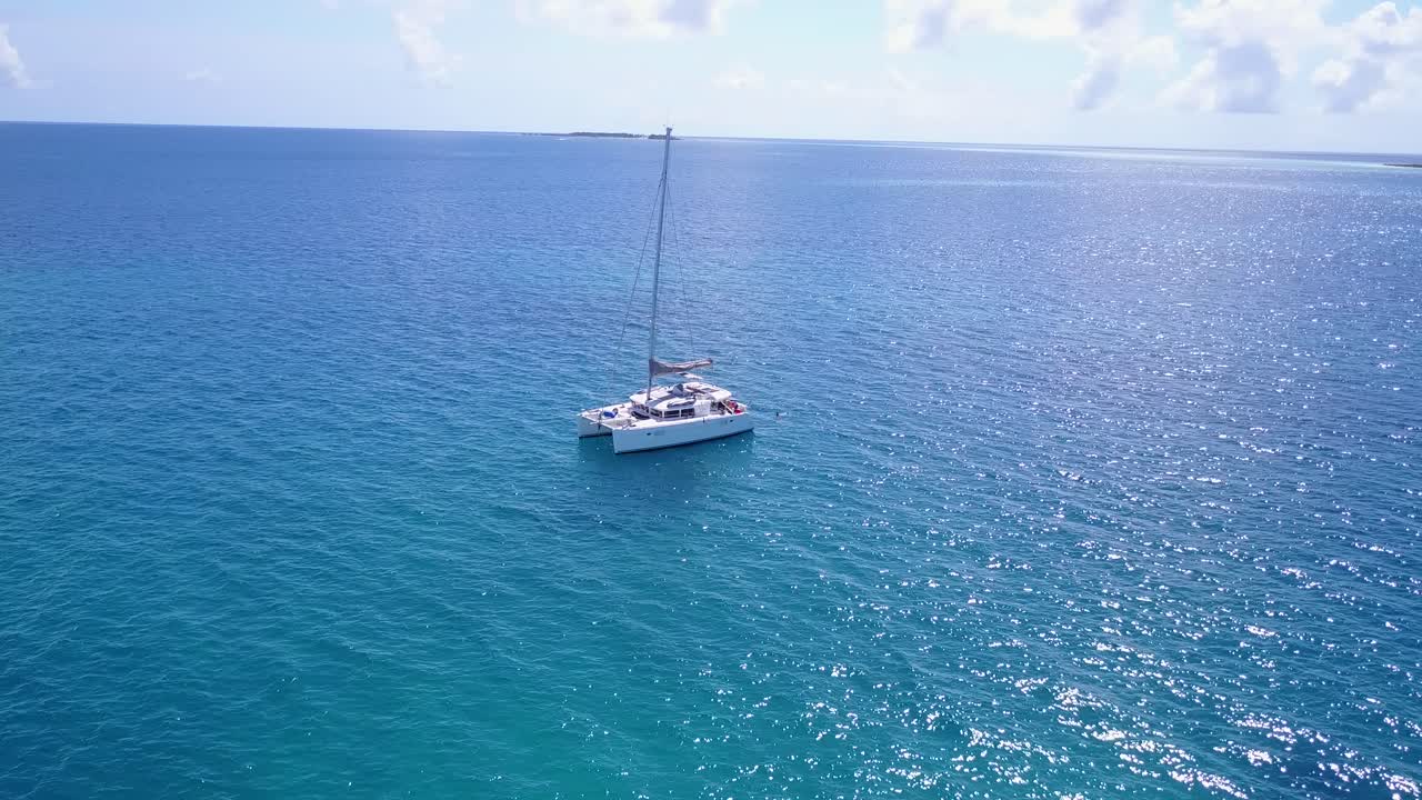 catamarán blanco anclado en aguas tranquilas de color azul celeste junto a una isla tropical con complejos turísticos y villas dentro de una exuberante vegetación en el caribe