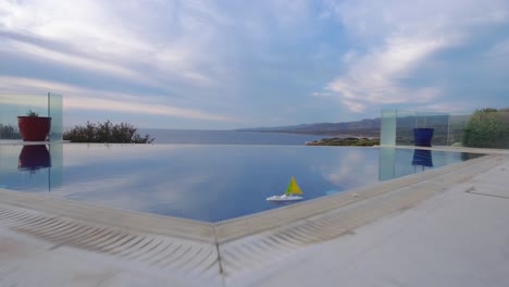 drone flies low over a pool past a bench with a canopy and a small toy boat in the pool