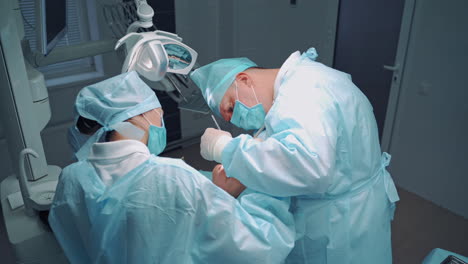 specialist man and female assistant in blue medical uniform are working in dental office. professional dentist and a nurse make an operation on teeth for client. oral treatment.
