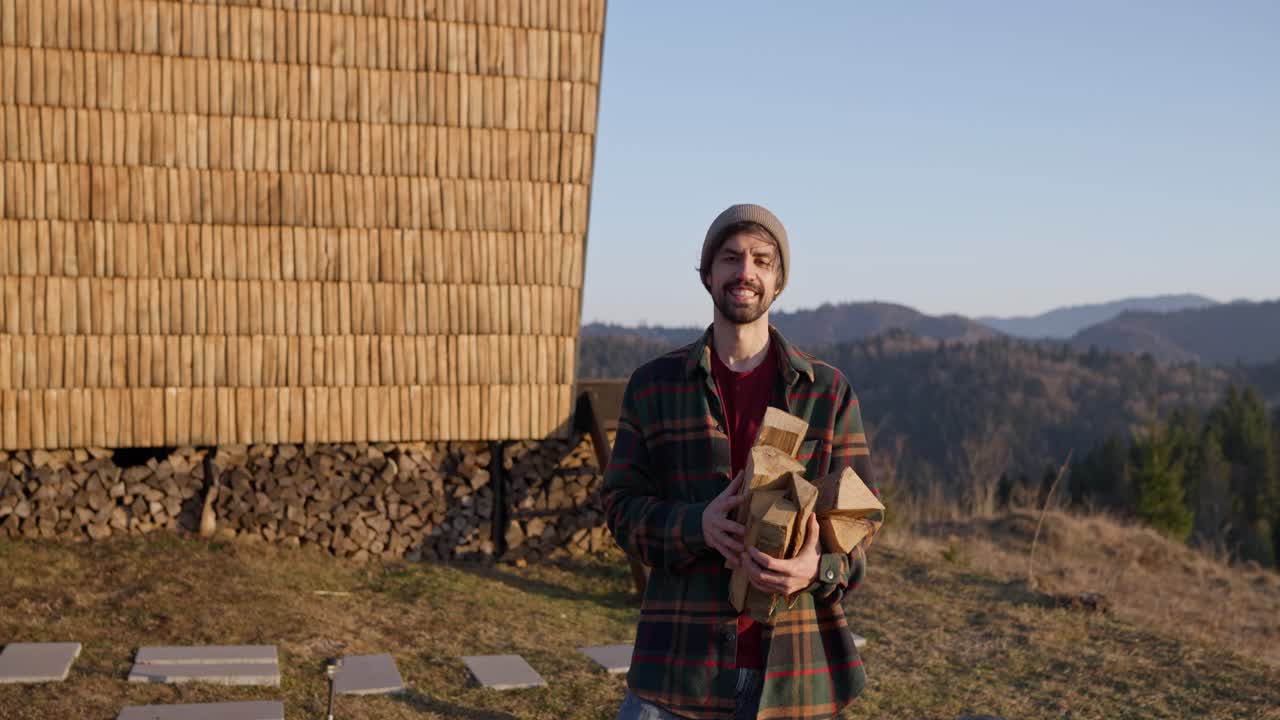 Man carrying firewood near a wooden house in the mountains