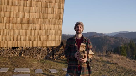 man carrying firewood near a wooden house in the mountains
