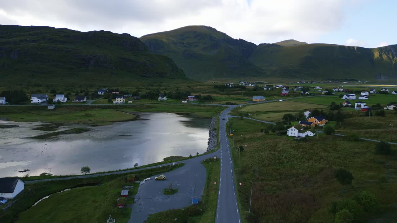 volando hacia abajo hacia la carretera de la calle en lofoten, noruega con la montaña de cuento de hadas circundante y el paisaje de hierba verde con pequeñas casas a lo largo de la carretera