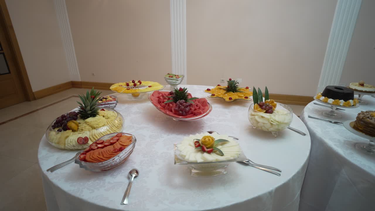 Round table with a vibrant fruit display, featuring watermelon, pineapple, and melon arranged elegantly, garnished with grapes and berries
