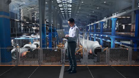 full body side view of an asian male professional worker standing with his laptop at the center of the wind turbine factory, typing on his laptop's keybaord with meditation