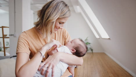 loving mother holding sleeping newborn baby son at home in loft apartment