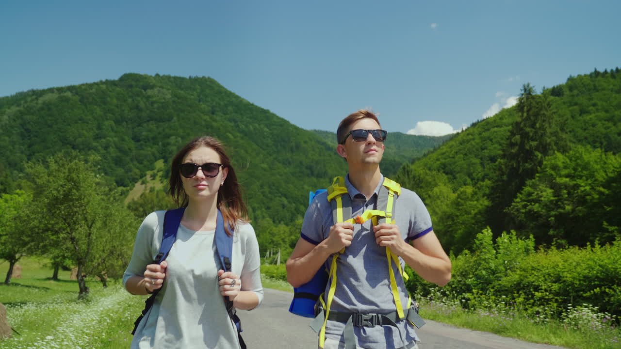 una joven pareja de turistas camina por el camino hacia hermosas montañas cubiertas de bosques forma activa de
