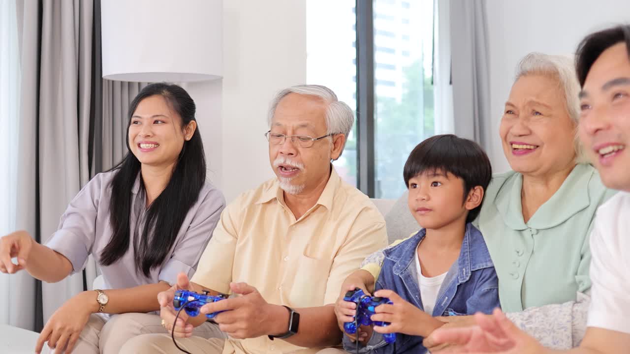 Multi-generational Asian family laughing and playing video games together in a bright, cozy living room