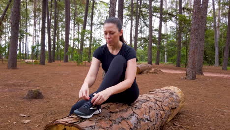 Kaukasische-Blonde-Frau-Sitzt-Auf-Einem-Umgestürzten-Baum-Im-Wald-Und-Bindet-Laufschuhe