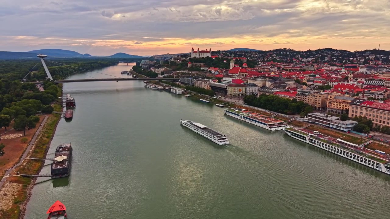 Udsigt over Donau-floden i Bratislava med både og byens skyline ved solnedgang med skyer på himlen