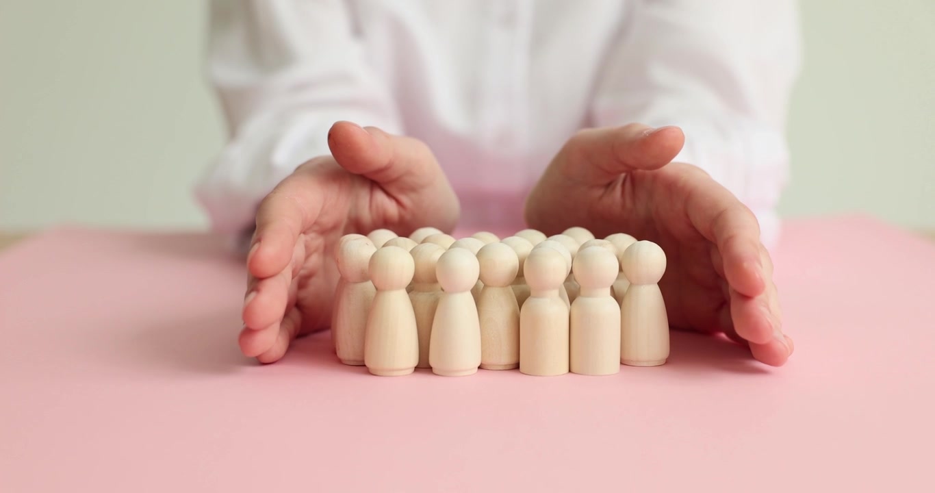 Manos de mujer ahuecadas alrededor de un grupo de figuras muy unidas.