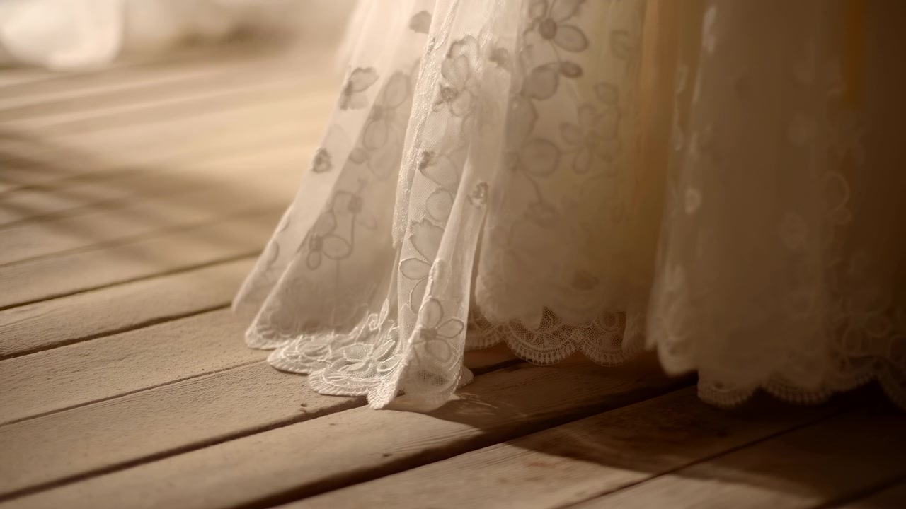 Close view of a white lace dress resting softly on warm wooden planks, with gentle sunlight, subtle shadows, and a calm elegant interior atmosphere