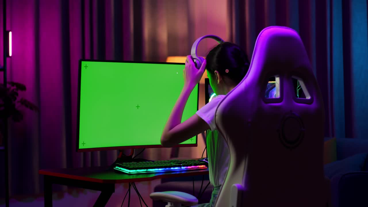 Adolescente asiatica gamer con le cuffie che inizia a giocare a un videogioco al computer con schermo verde per mockup.