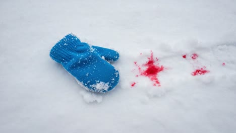 a mysterious scene unfolds: a blue mitten lies abandoned in the snow, surrounded by stark red splashes, evoking intrigue and unanswered questions about what happened here