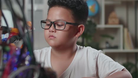 close up of satisfied asian cute boy looking and checking a cyborg hand while working on a laptop at home