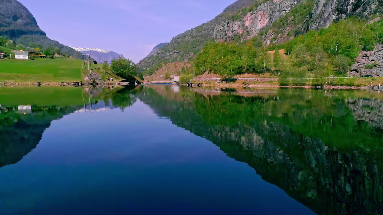 낮에는 산맥으로 둘러싸인 그림 같은 호수 기슭을 따라 위치한 전통 가옥이 있는 마을의 공중 드론 뒤로 이동 샷