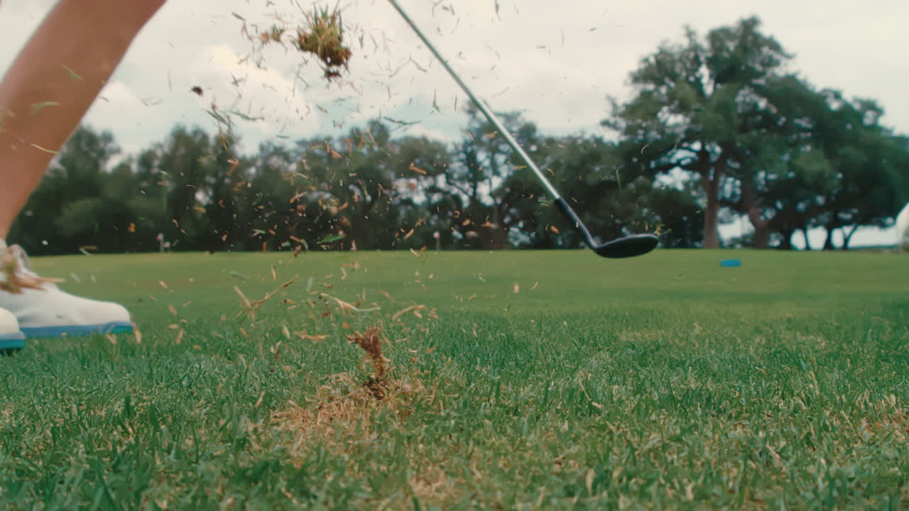 Extreme slow-motion view from behind of golfer’s chip shot. Grass and divot fly on contact, showcasing precision, technique, and dynamic short game action on golf course